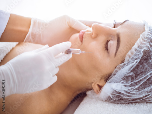 Beautician doing beauty procedure with syringe to face of young brunette woman in sunny spa center. Cosmetic medicine and surgery  beauty injections