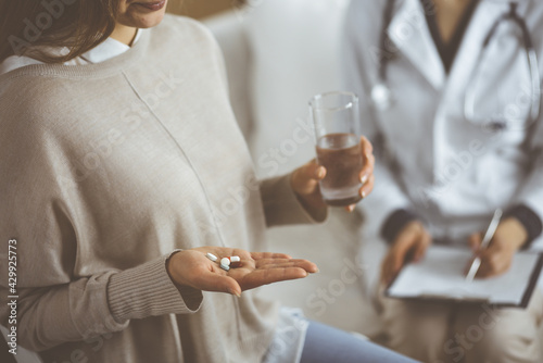 Close-up woman-patient holding pills near her doctor, time to take medications, cure for headache or remedy pain killer drugs. Stay at home concept during Coronavirus pandemic and self isolation photo