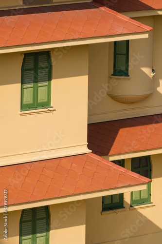 High angle view of flat concrete roof tiles with green wooden windows on yellow cement wall of vintage building in vertical frame
