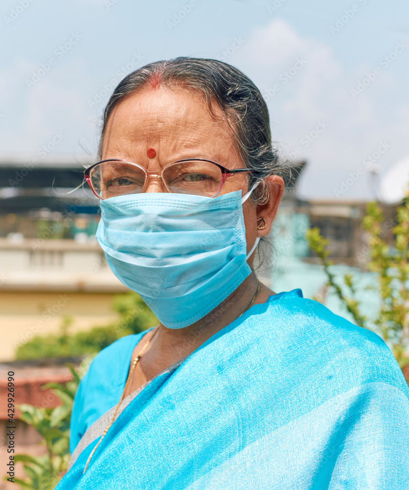 Portrait of an aged Indian woman, wearing traditional blue coloured Indian sari and surgical