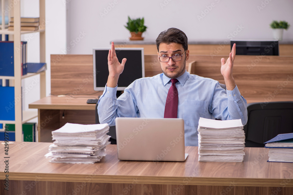 Young male employee unhappy with excessive work in the office Young male employee unhappy with excessive work in the office