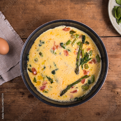 Cooking omelette with asparagus, tomatoes and spinach - mixed eggs poured into the pan with asparagus, tomatoes and spinach.