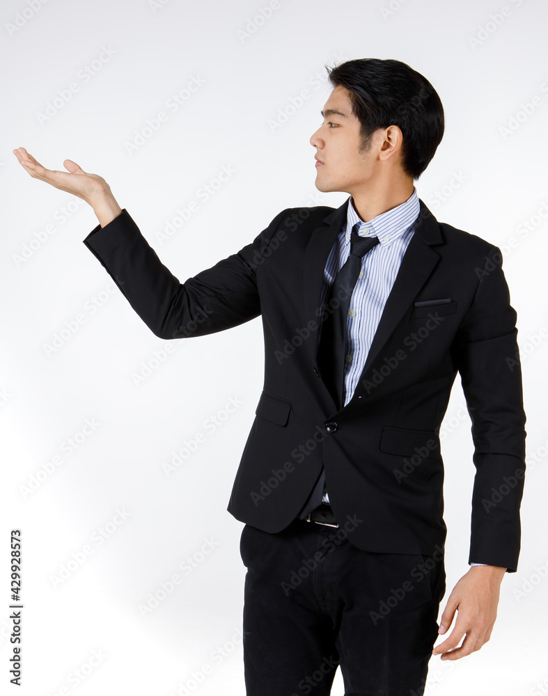 Portrait shot of Asian young happy successful marketing officer employee in modern style black formal suit standing smiling hold empty hand up presenting promoting product in front white background Portrait shot of Asian young happy successful marketing officer employee in modern style black formal suit standing smiling hold empty hand up presenting promoting product in front white background