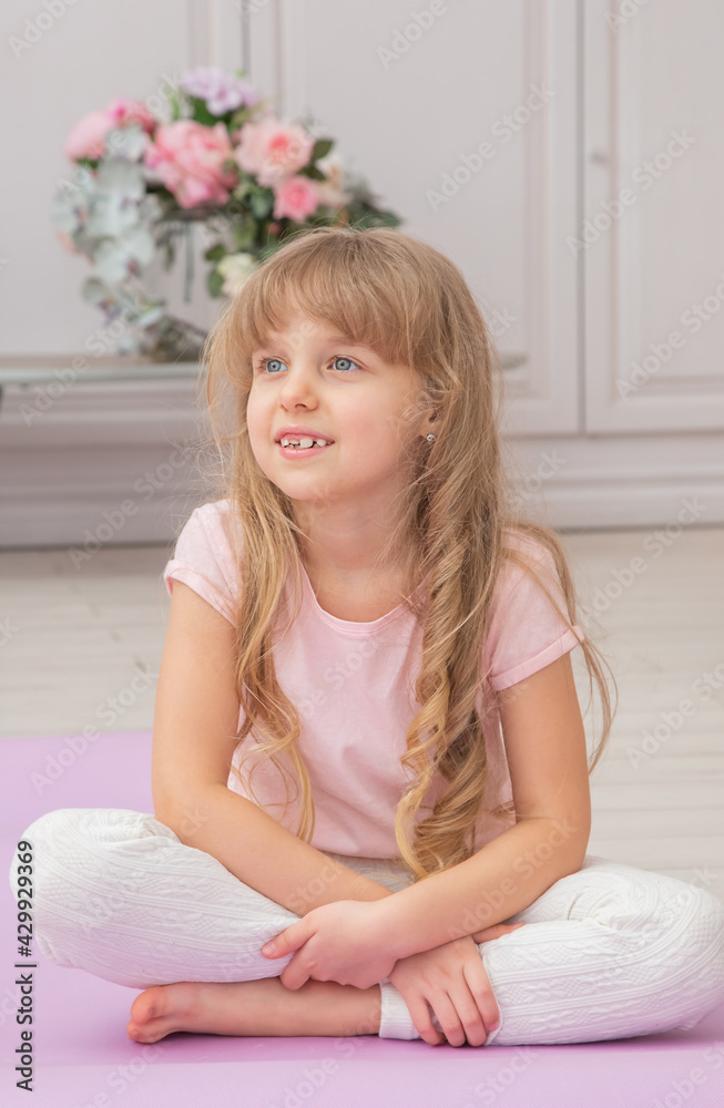Full length front view cute little preschool girl sitting on on yoga mat