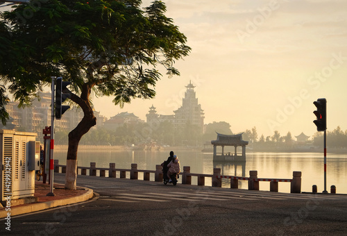 Chinese woman is riding with her daughter behind near central city garden pool at Xiamen city in the morning 