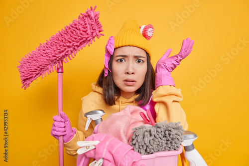 Foto Disappointed busy housewife being angry with children who make mess in house holds mop does laundry looks displeased as has much work to do isolated over yellow background