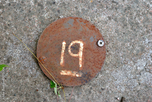 Close Up of Circular Rusty Metal Plate with Number 19 Painted in White