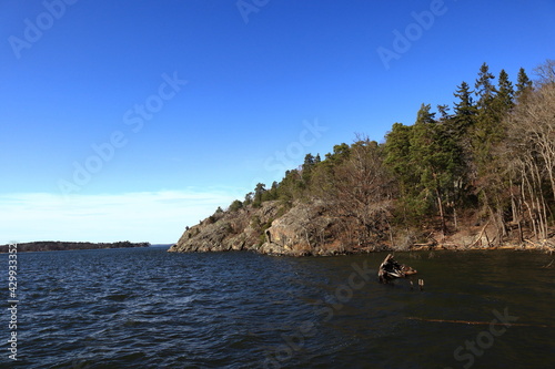 One old wooden shipwreck in the Swedish lake Mälaren or Malaren. Mountain with cliffs and trees in the background. Nice day and view outside at spring time. Järfälla, Stockholm, Sweden, Europe.
