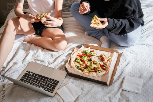 Girls sitting at the bed and eating pizza at the free time at home