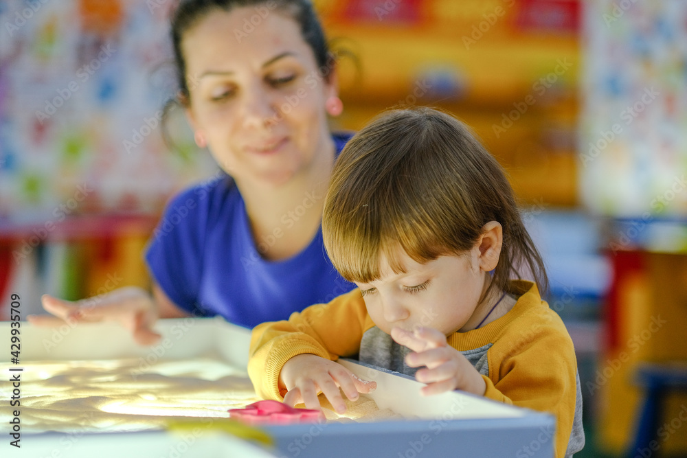 Fototapeta premium Creative early baby development. A mother teaches her child to draw with her fingers in the sand. Center for the Development of Children with Autism.