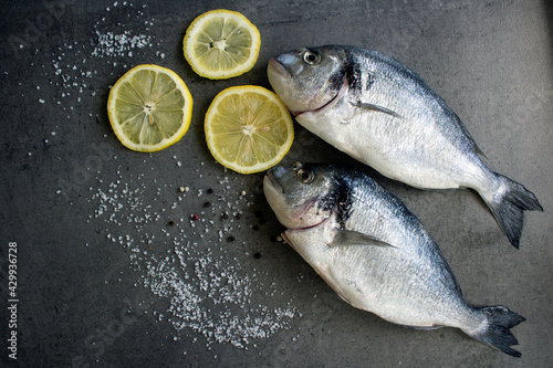 Sea bream dorado fish with lemon and salt on gray textured background with copy space. Uncooked fish top view photo. Balanced diet concept. 