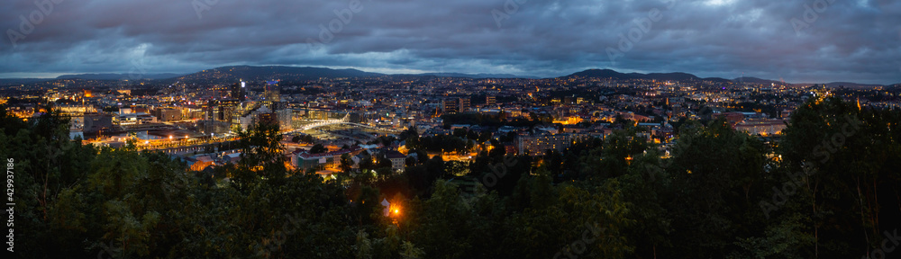 Night panoramic view of Oslo, capital of Norway. Dark cloudscape ower capital of Norway. Scandinavian city with lighted buildings and bridges, surrounded by forests.