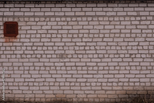 A white brick wall  blackened with age. Ventilation window.