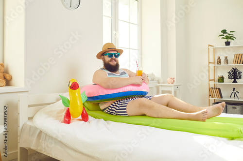 Funny positive smiling bearded man with beach accessories lying in bed imagining travel to resort on vacation enjoyment. Quarantine lockdown, stay home, social distancing, trip canceled by coronavirus