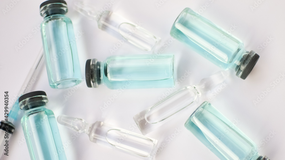 Vial vaccine, top view of glass ampoules with transparent and blue liquid lying on white background, global vaccination concept