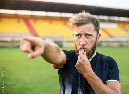 A handsome football referee with a beard plays the whistle photo