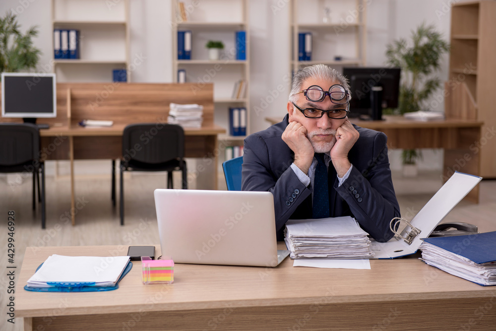 Old male employee auditor wearing many glasses at workplace Old male employee auditor wearing many glasses at workplace