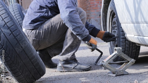 screwing in bolts to fix the wheel on the car by a person with a crank in his hand, a small jack and wheels next to the machine on which the wheel is installed, self-change of rubber