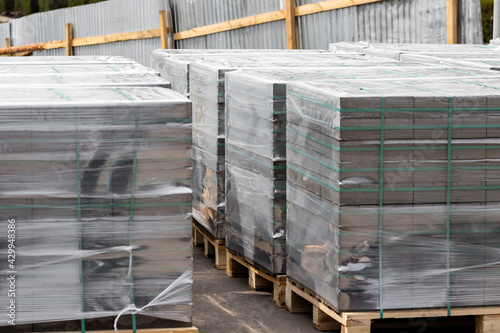 New film-wrapped building materials on pallets neatly stacked kerb paving stone and gray brick for the industrial street finishing of parks and streets of the city. High quality photo