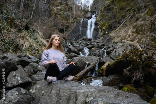 Girl sits on a tree and meditates near mountain river in Abkhazia