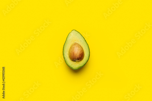 fresh ripe half of an avocado with a bone on a bright yellow background. Top view, flat lay
