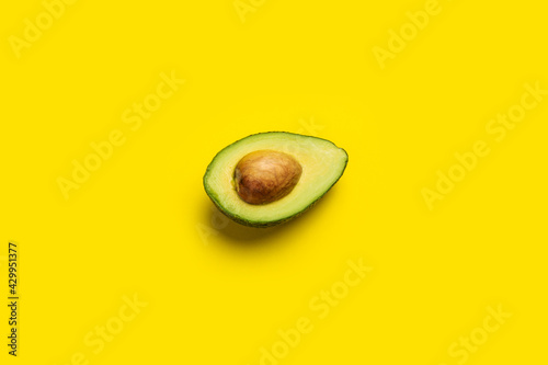fresh ripe slice, half an avocado on a bright yellow background. Top view, flat lay