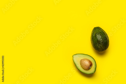 Whole and half an avocado on a bright yellow background. Top view, flat lay