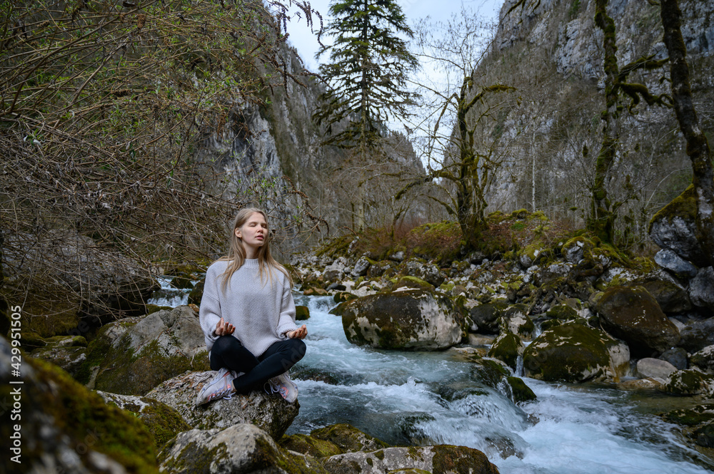 Girl sits on a tree and meditates near mountain river in Abkhazia Girl sits on a tree and meditates near mountain river in Abkhazia