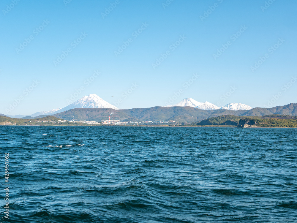 The seaport in the Avacha Bay of Petropavlovsk-Kamchatsky. View from the sailing yacht to the seaport, volcanoes, autumn hills against the blue sky. Kamchatka Peninsula, Russia.