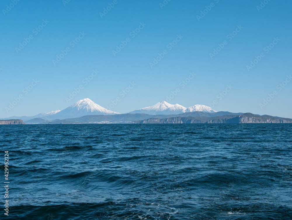 Exit on a yacht to the Avacha Bay of the Pacific Ocean. View from the sailing yacht to the seaport, volcanoes, autumn hills against the blue sky. Kamchatka Peninsula, Russia.