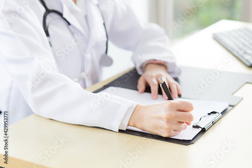 A female doctor is writing a report on a patient s condition in a hospital examination room.