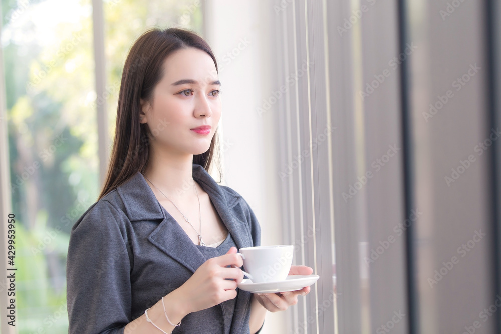 Asian working woman is looking out of window to think something while holds coffee cup in her hand. Asian working woman is looking out of window to think something while holds coffee cup in her hand.