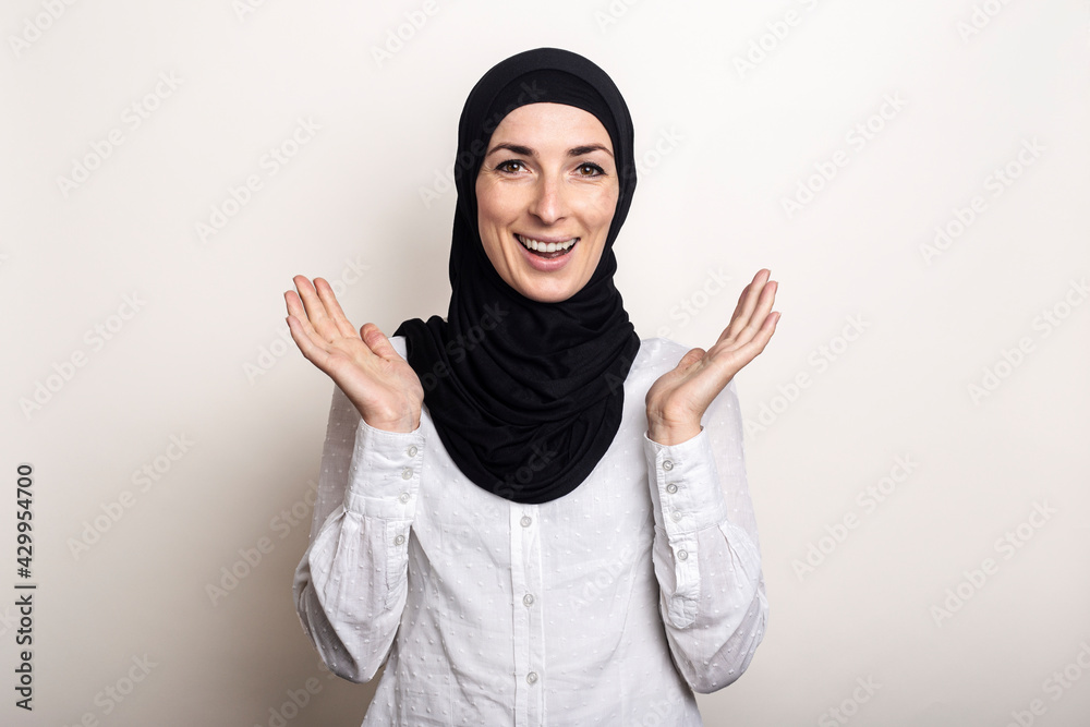Young woman with surprised face in white shirt and hijab on light background