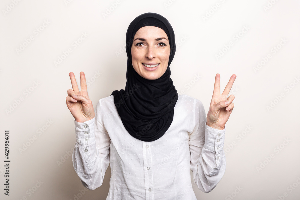 Young woman with crossed arms dressed in a white shirt and hijab shows a welcome gesture All is well on a light background. Banner Young woman with crossed arms dressed in a white shirt and hijab shows a welcome gesture All is well on a light background. Banner