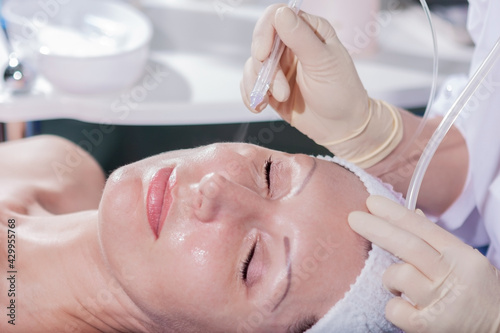 Mature woman having jet peeling facial therapy treatment in beauty clinic 