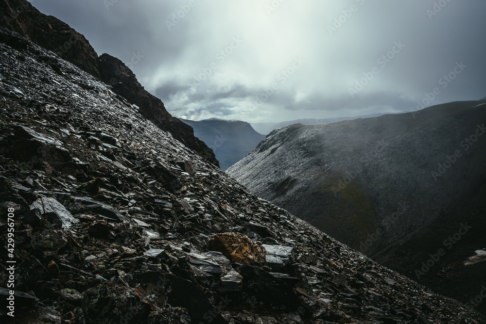 Dark atmospheric landscape on edge of abyss in highlands. Dangerous mountains and abyss in overcast weather. Danger mountain pass and sharp rocks under gray sky. Dangerous rainy weather in mountains.