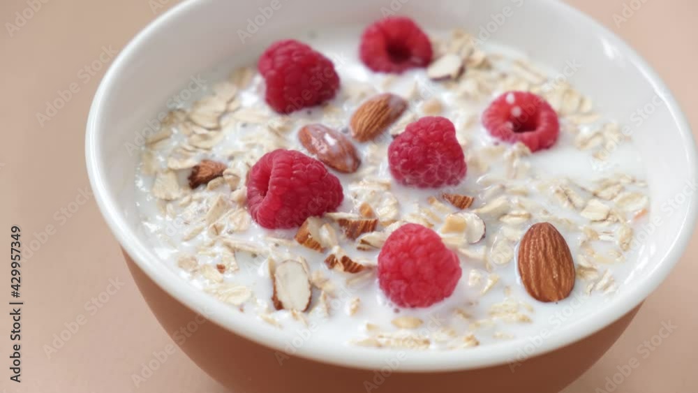 Milk pouring in a bowl with oat muesli. Healthy breakfast food, oatmeal bowl with raspberries and almonds Milk pouring in a bowl with oat muesli. Healthy breakfast food, oatmeal bowl with raspberries and almonds