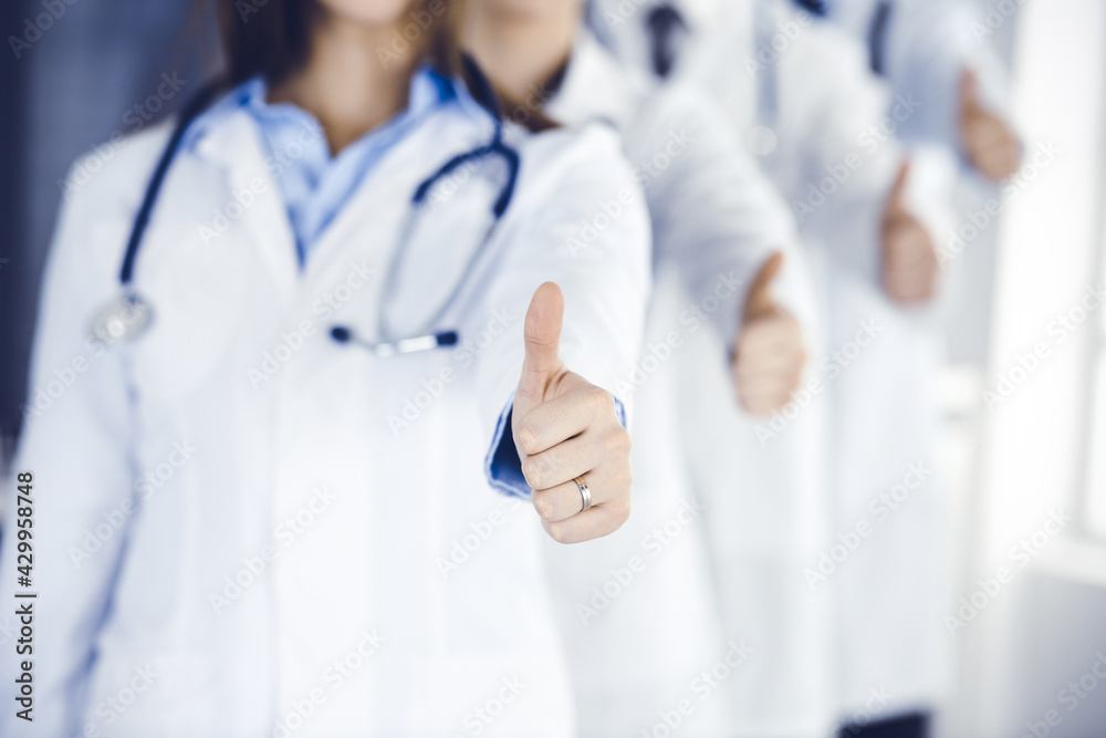 Group of modern doctors standing as a team with thumbs up in hospital office. Medical help, insurance in health care, best desease treatment and medicine concept Group of modern doctors standing as a team with thumbs up in hospital office. Medical help, insurance in health care, best desease treatment and medicine concept