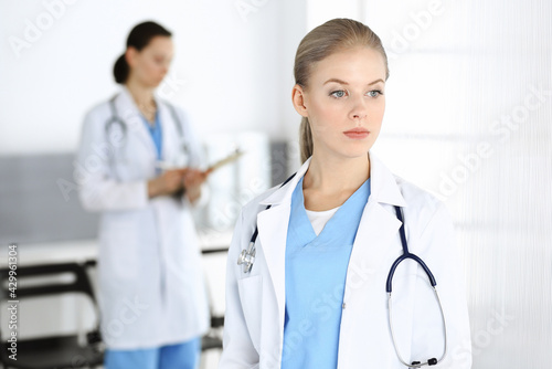 Woman - doctor standing in clinic with colleague at the background. Physician at work. Medicine and health care concept