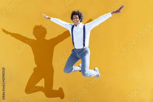 Black man with afro hair jumping on a yellow urban background