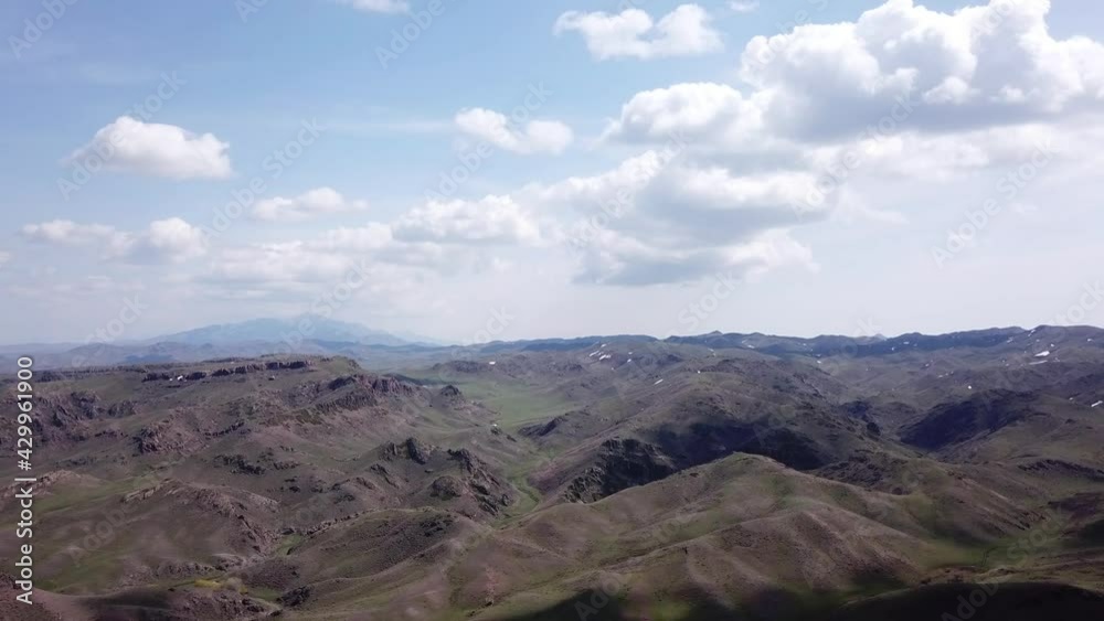 The shadow of the clouds runs over the green hills. In the distance you can see the mountains, the river, the road. Hills covered with grass. Small gorges. Pure nature. Top view from drone. Kazakhstan