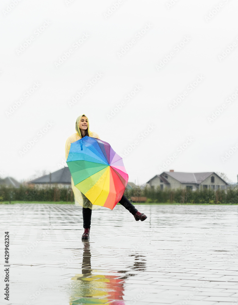 Beautiful brunette woman holding colorful umbrella dancing in the rain