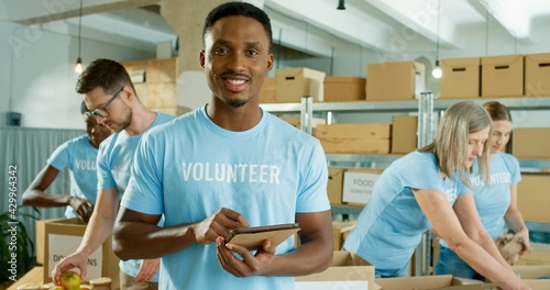 Εκτύπωση καμβά Close up portrait of cheerful young African American handsome man in good mood work in charity center, volunteer tapping on tablet and smiling at camera
