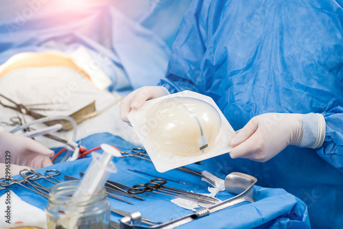 Surgeon in operation room is holding sterile breast silicone implant in hands.