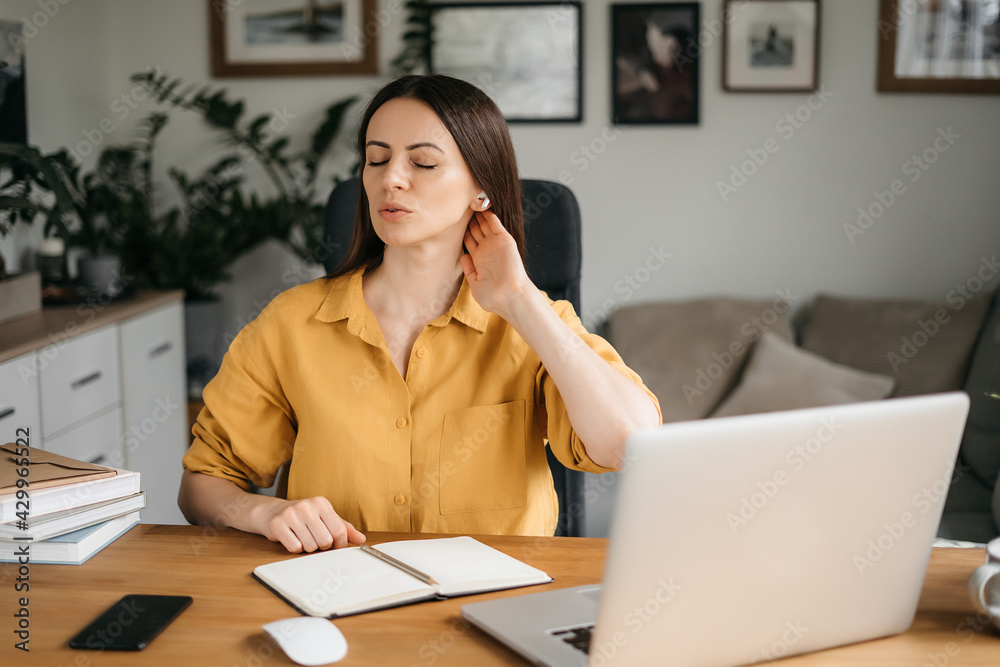 Smiling business woman talking on a mobile phone and using a laptop while working at home, looking at the screen, reading a message, a young female employee advises a client, telephone conversations