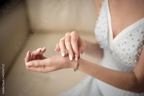 A beautiful young bride in a white long dress touches a gold bracelet on her arm with her hand. Blue, yellow, white, gold, beige.