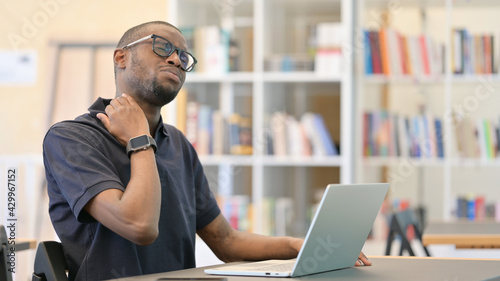 Hardworking Young African Man with Laptop having Neck Pain in Library