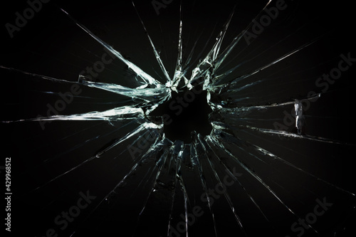 The hole in the broken and cracked glass, closeup on dark background