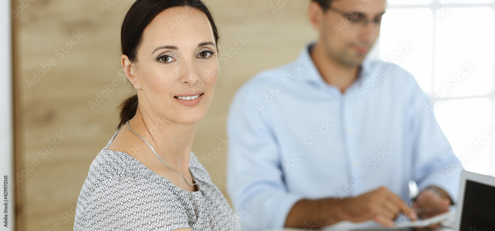 Fototapeta premium Businesswoman and businessman discussing questions while using a computer in modern office. Portrait of female latin american entrepreneur at meeting. Group of diverse people