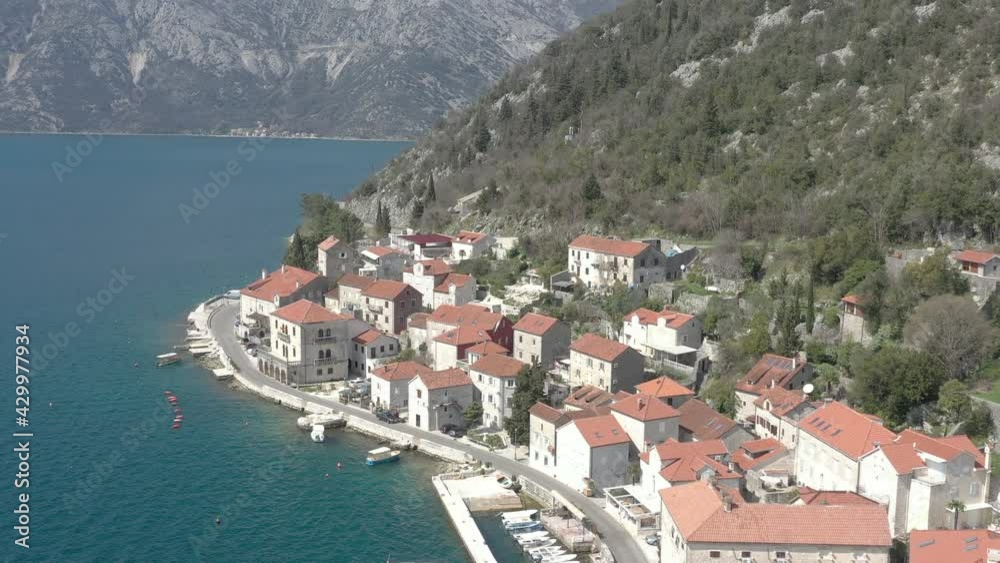 Aerial view of Montenegrin seaside town. Flying above the sea and coastline. Ancient Balkans traditional architecture – white stone buildings with red roofs, ancient Christian church and mountains in Aerial view of Montenegrin seaside town. Flying above the sea and coastline. Ancient Balkans traditional architecture – white stone buildings with red roofs, ancient Christian church and mountains in